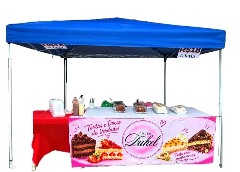 Barraca da Doces Dukel com toldo azul, balões rosa e a mesa de tortas