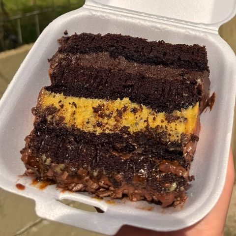 Fatia na embalagem com massa de chocolate, uma camada amarela cremosa no meio e base crocante de chocolate